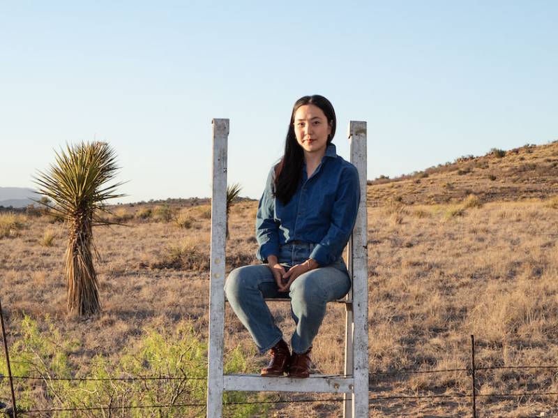A Korean woman in denim with long hair sits on a structure in a desert landscape.