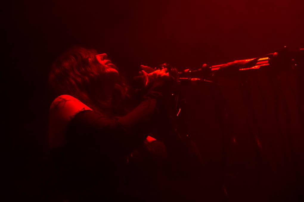A woman tilts her head back while holding onto a microphone. She is dimly lit in red light.