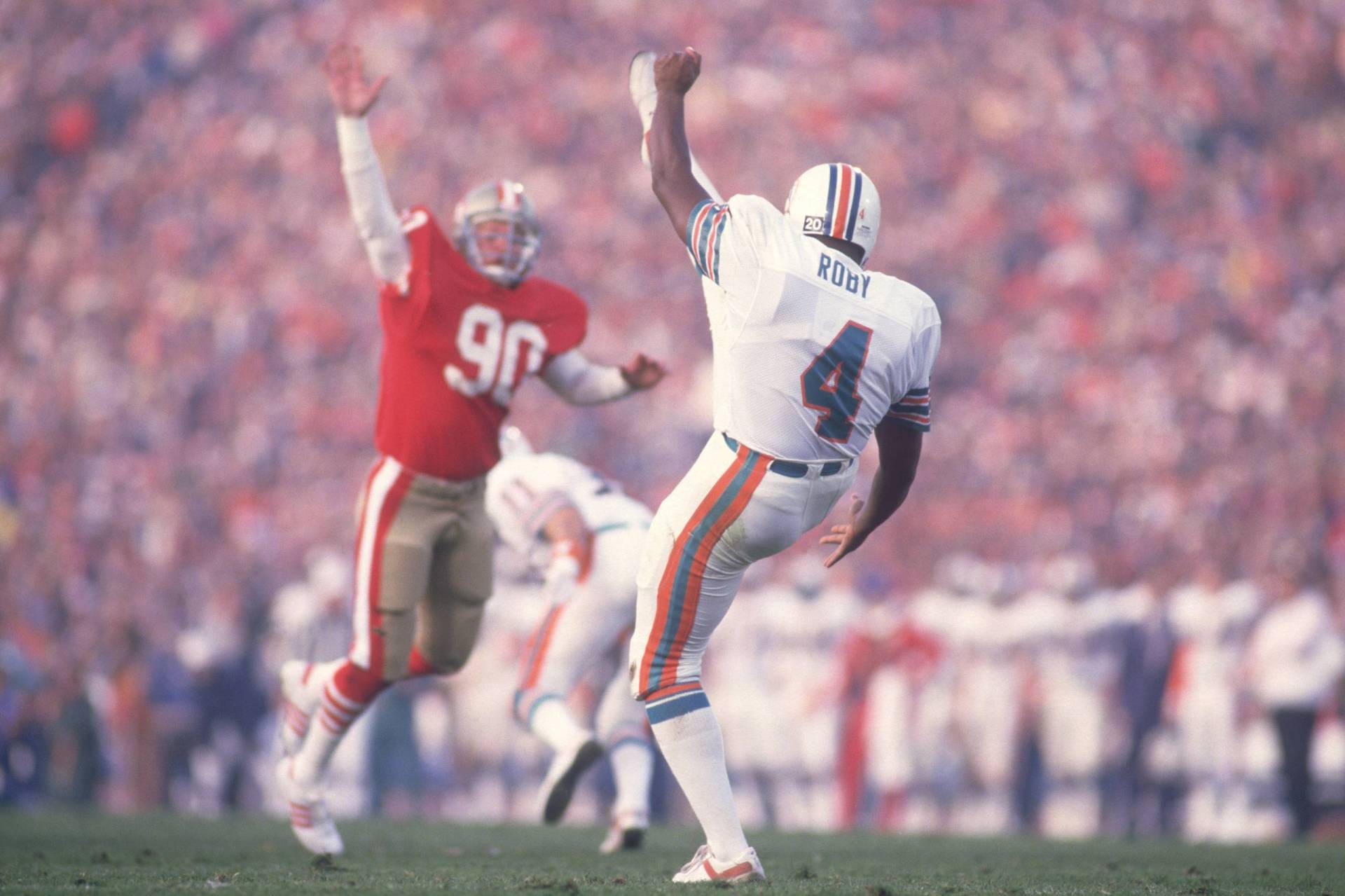 Football players from opposing teams face each other with one arm raised, their bodies slightly off the ground.