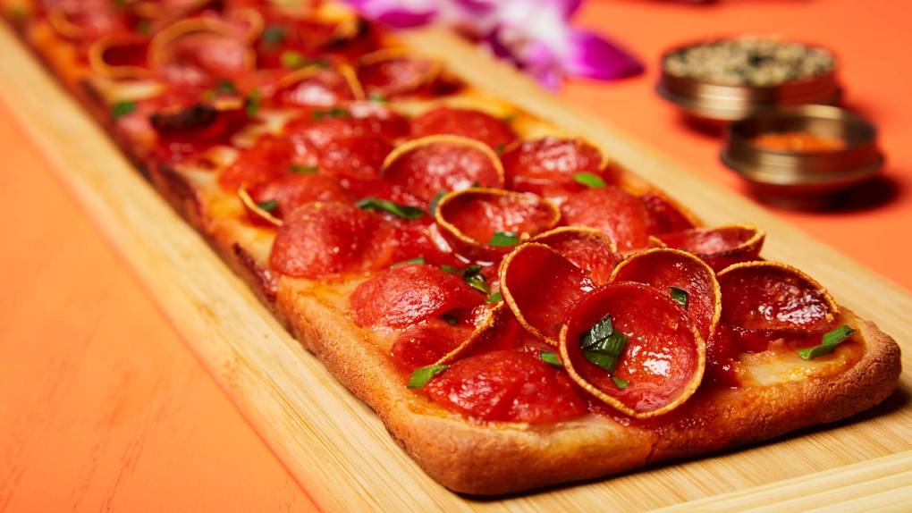 A long, rectangular pepperoni pizza, served on a wooden board.