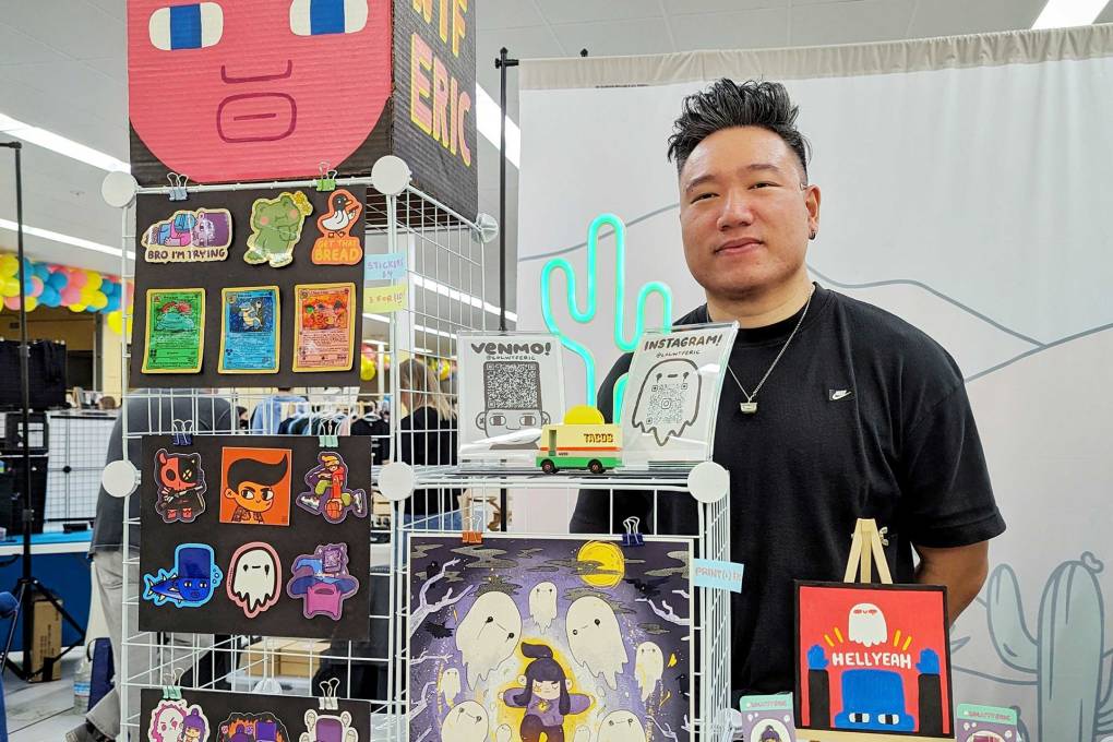 An artist vendor stands at his booth of stickers and art prints.