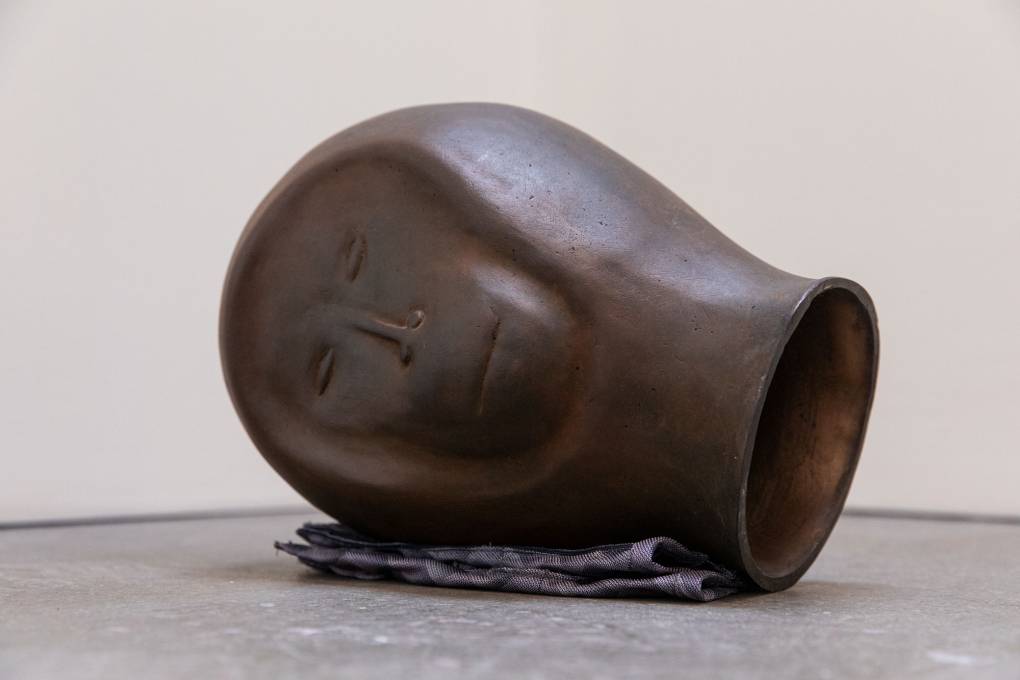 Simplified, hollow metal sculpture of chimpanzee's head resting on its side on folded cloth