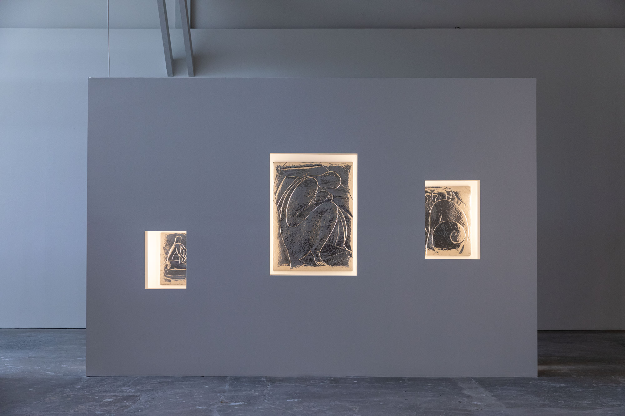 White wall with three embedded and lit metal reliefs