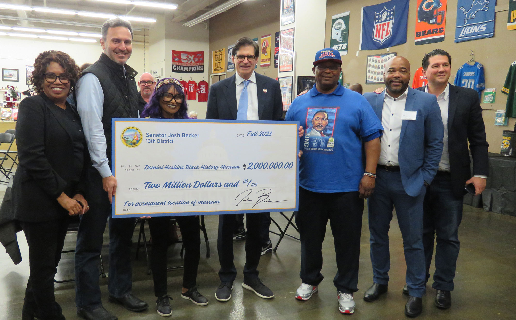 Group of seven people smiling and holding giant check