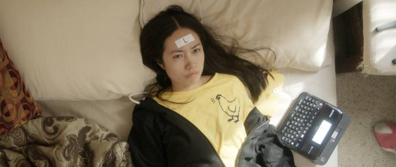 Woman seen from above in bed with "L" sticker on her forehead