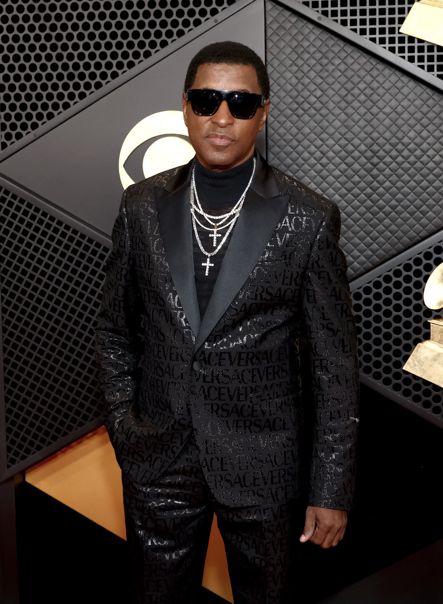 A Black man wearing a shiny black Versace suit and sunglasses.