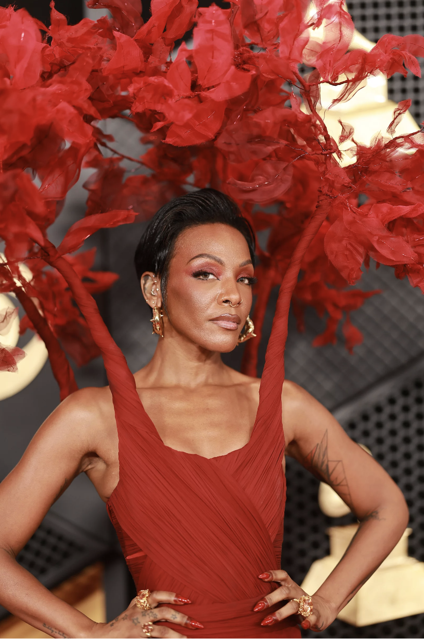 A Black woman wearing a red gown with structured straps that sprout into feathers over her head.