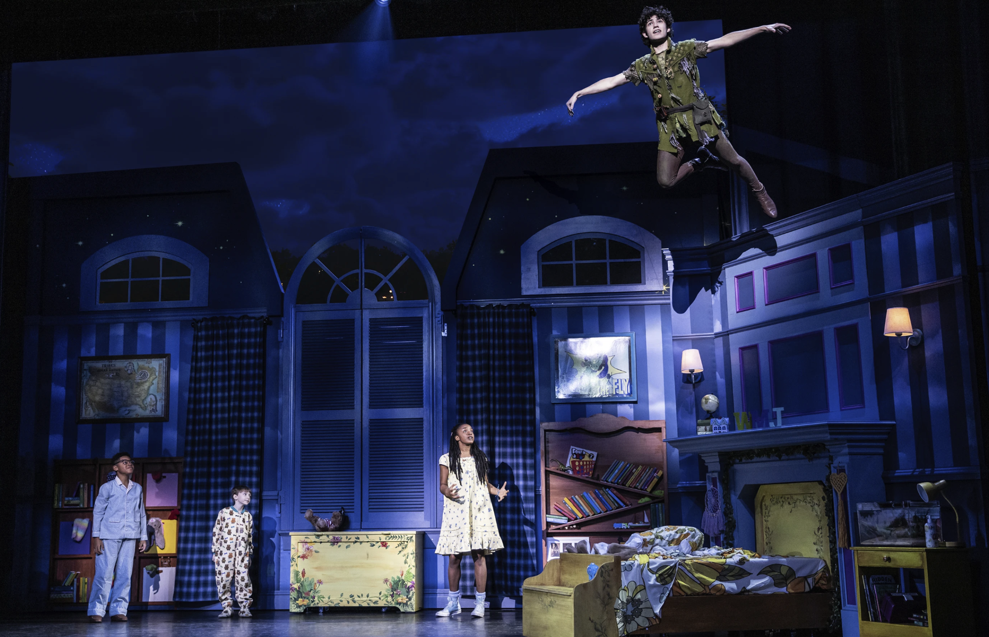 A stage set with three children wearing pajamas on stage and one child flying over their heads.