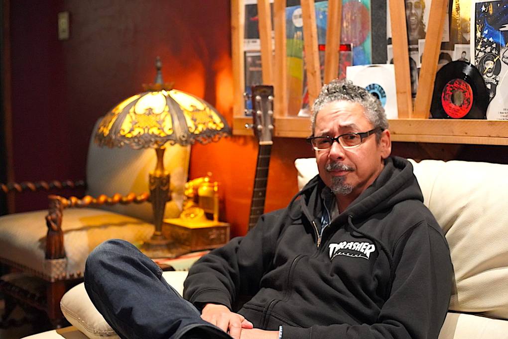 Superstar skateboarder and talented musician, Tommy Guerrero sits inside of a studio in Berkeley, wearing a black Thrasher hoodie and glasses.