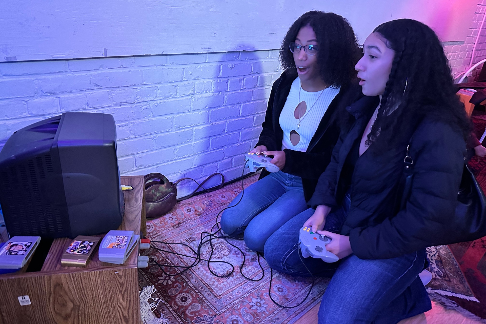 Two people kneel in front of a small TV screen while holding video game controllers.