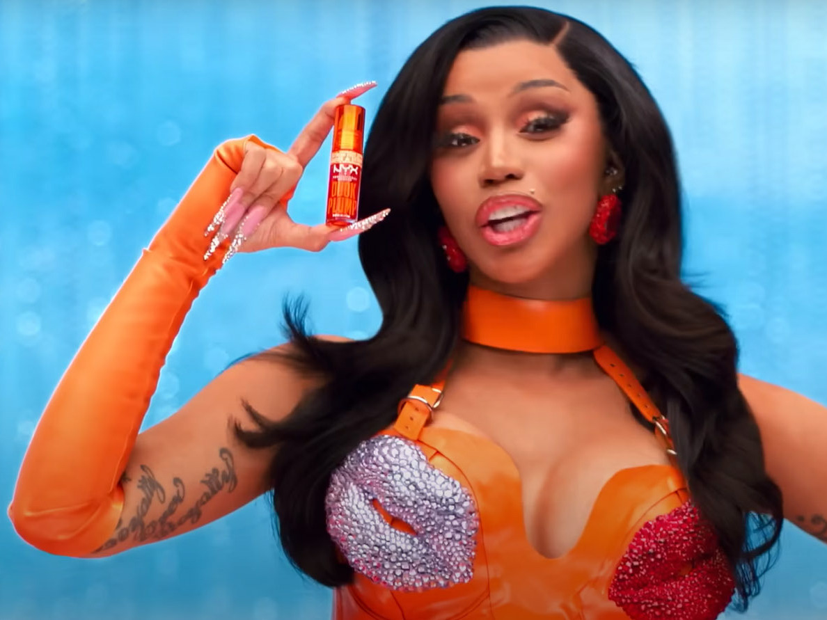 A Black woman with very long nails holds up a lipstick.