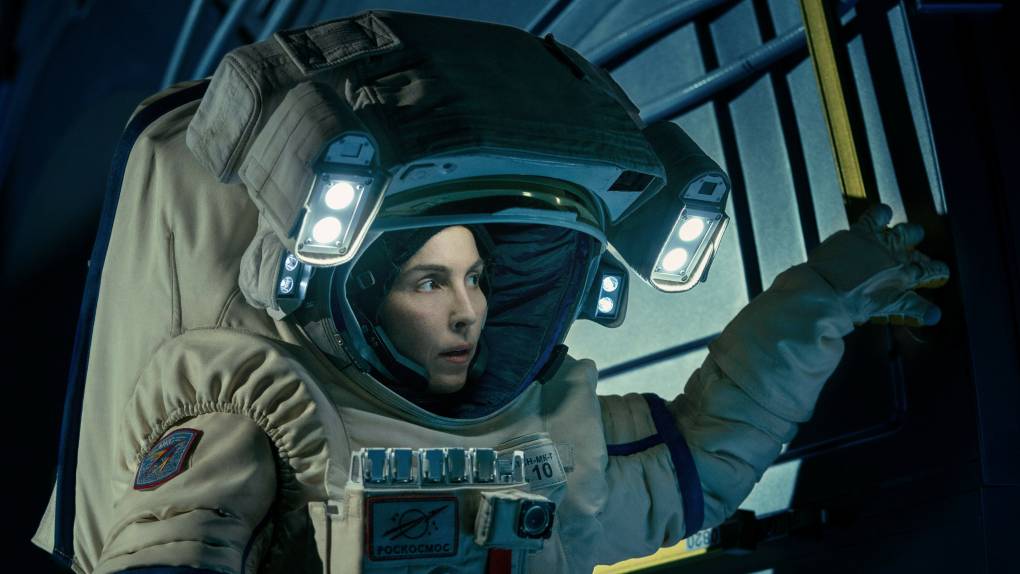 A woman peers out from inside a very large astronaut suit.