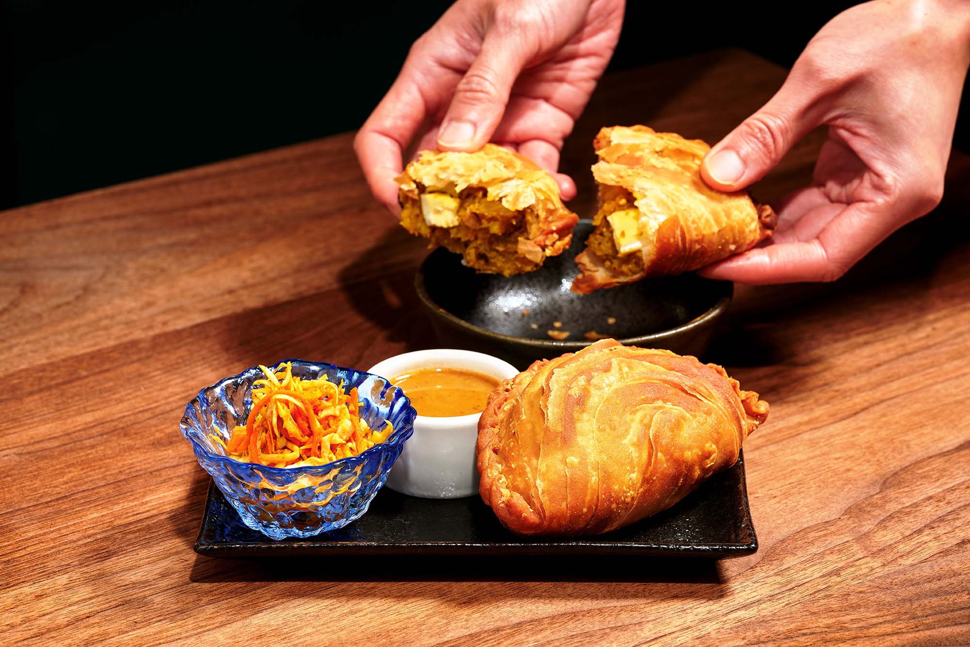 Two hands break apart a curry puff.