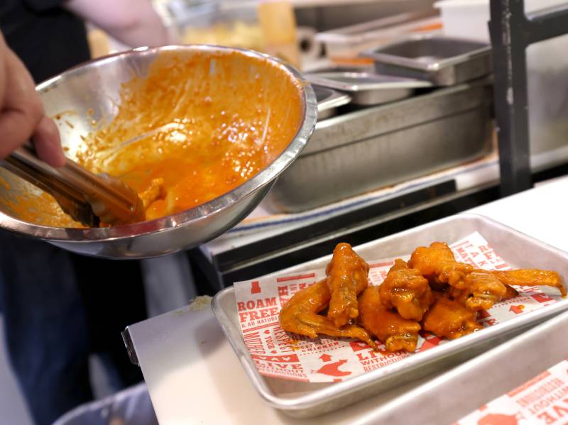 A plate of chicken wings sits next to a stove. Someone holds a bowl of sauce over the plate.
