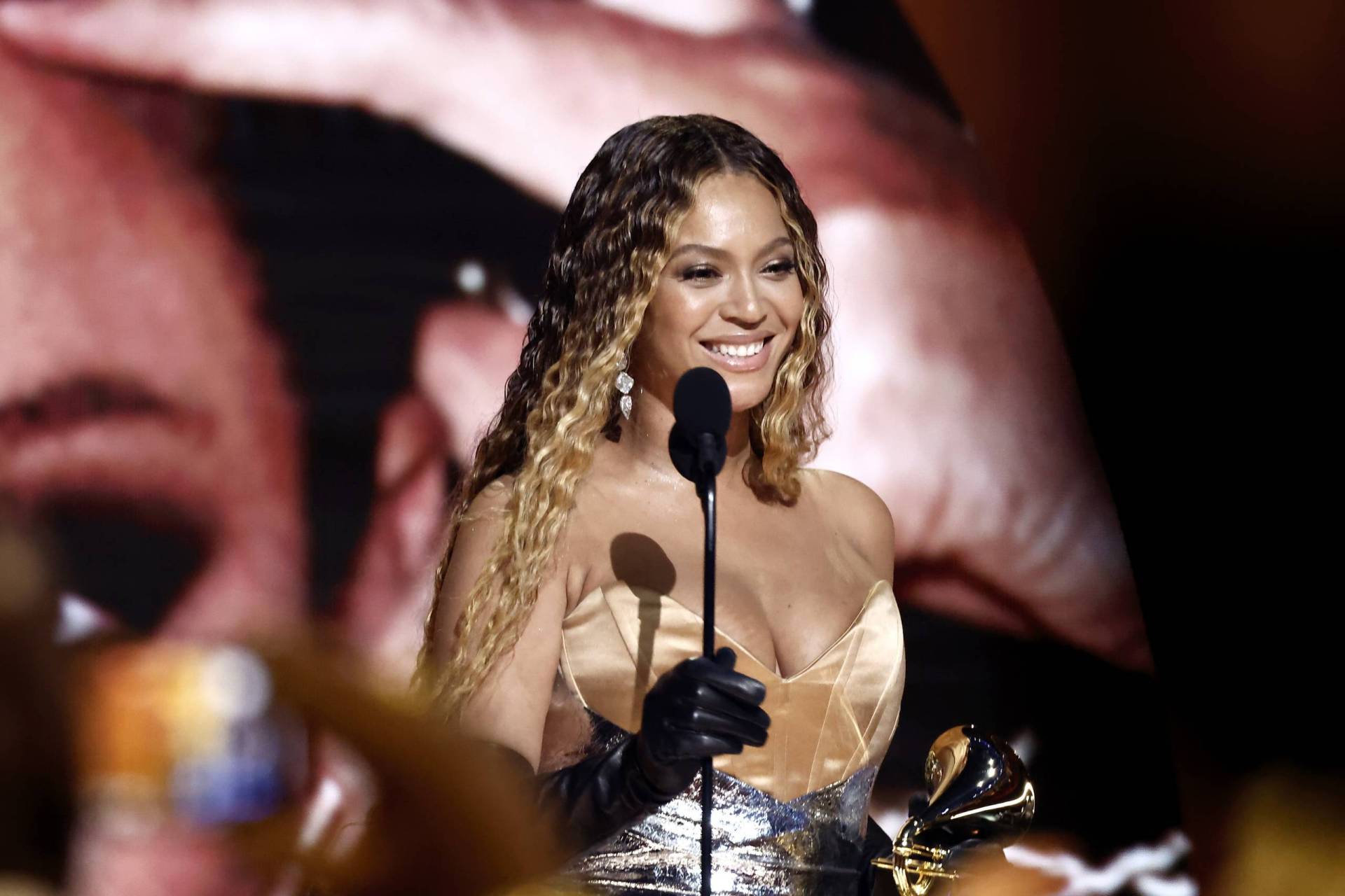 A Black woman wearing a gown stands on stage accepting an award. She is smiling.