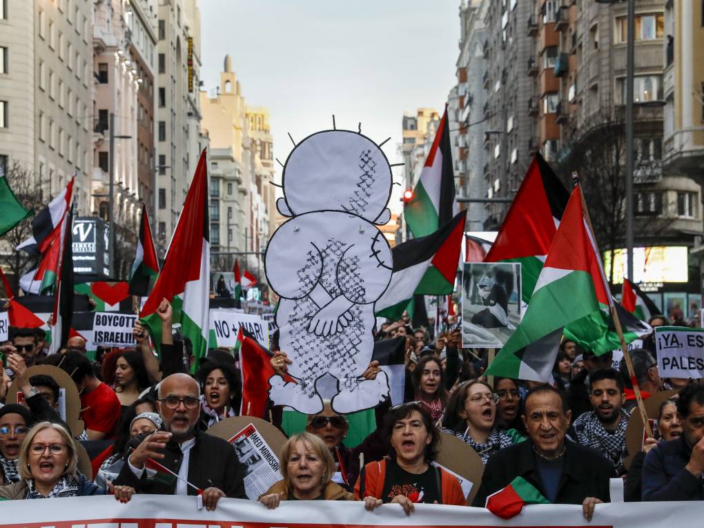 A protest march, people waving Palestinian flags and a cardboard cutout of a boy with his back turned.