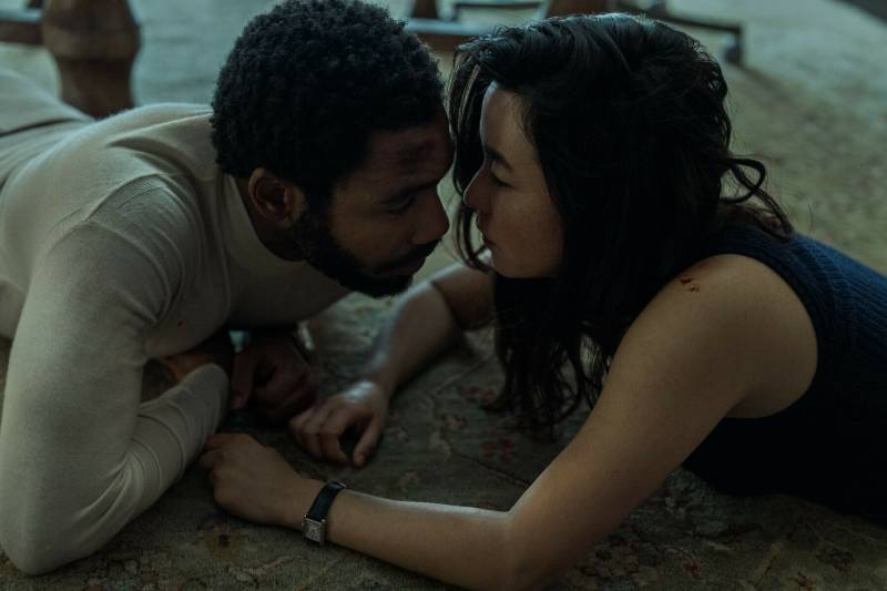 A Black man and Asian woman lie on the floor, face to face and very close.