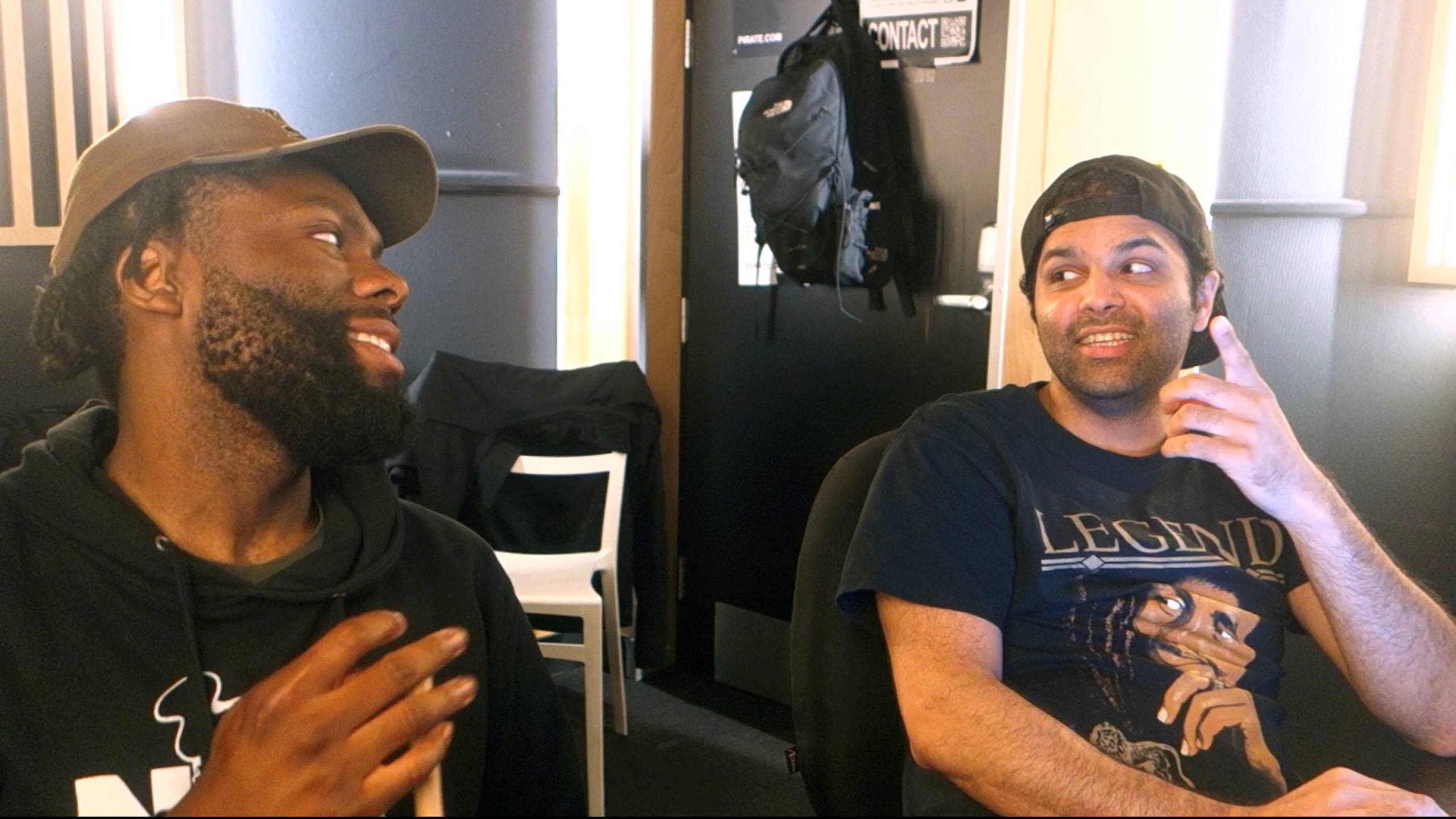 Two collaborators smile at each other in a music studio.