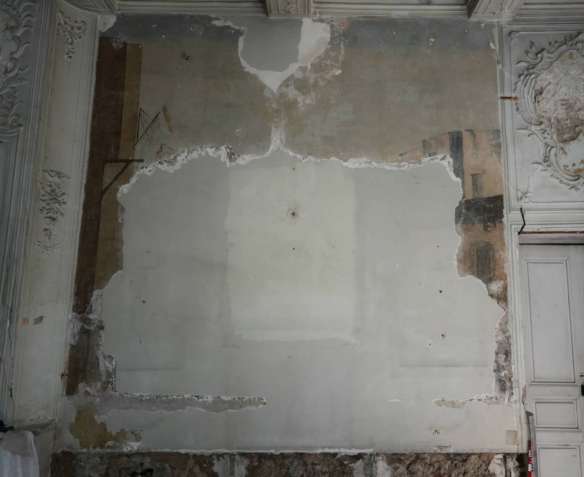 An unfinished white wall with a partial view of a wall painting of sky and buildings behind it.