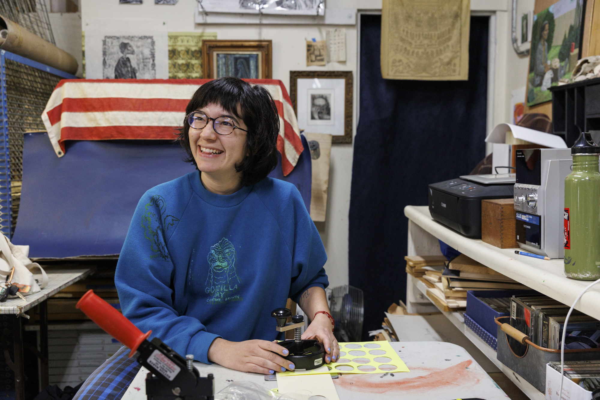 Smiling person in blue sweatshirt uses a button-maker