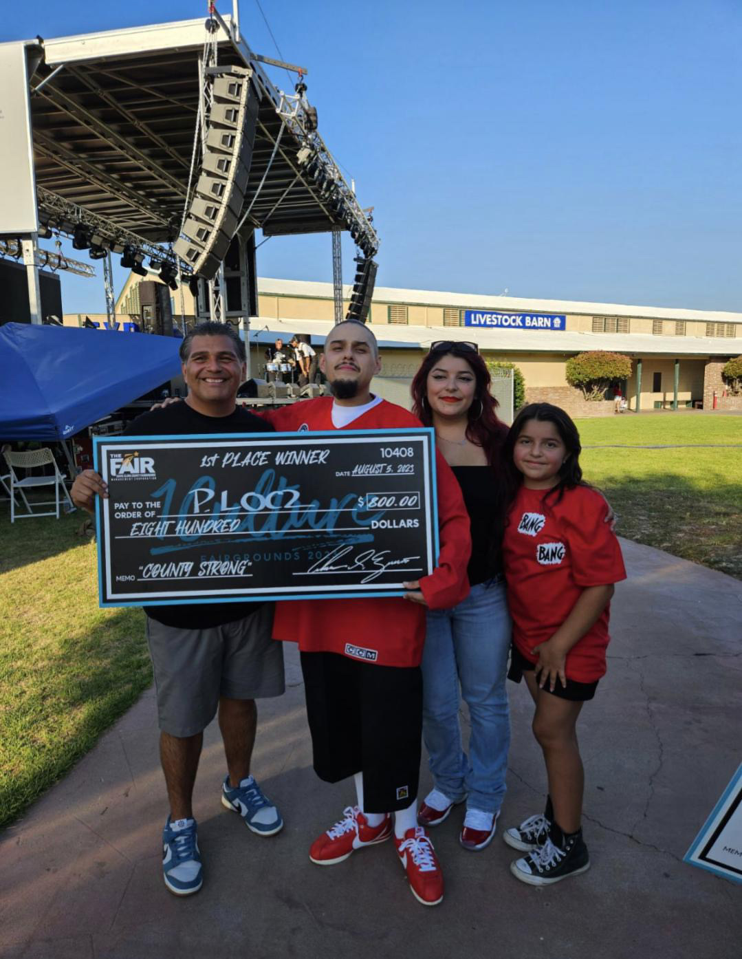an artist stands with his family and an art gallery owner after receiving a check for winning first place in an art contest