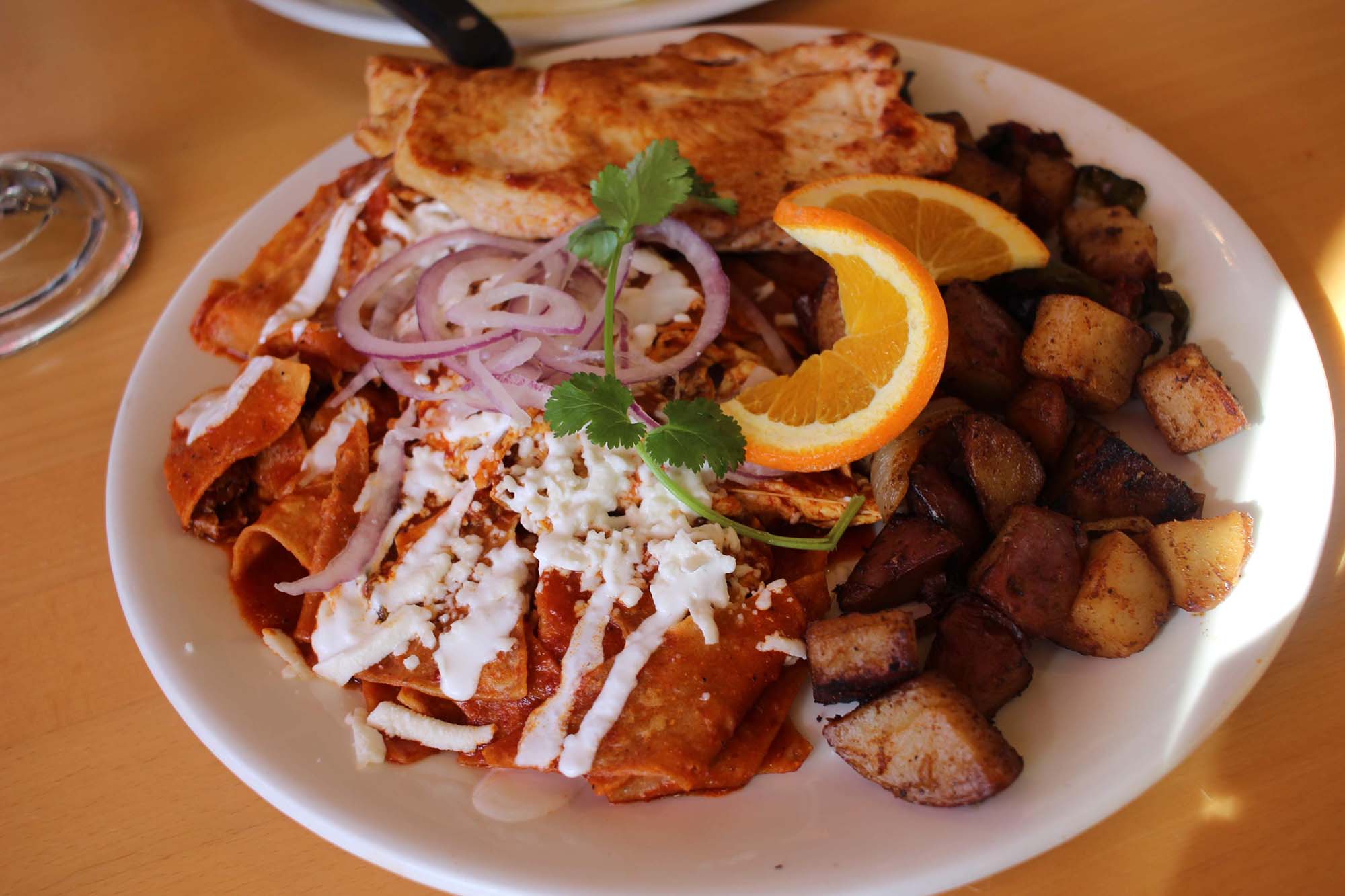 A plate of red chilaquiles with a side of breakfast potatoes.