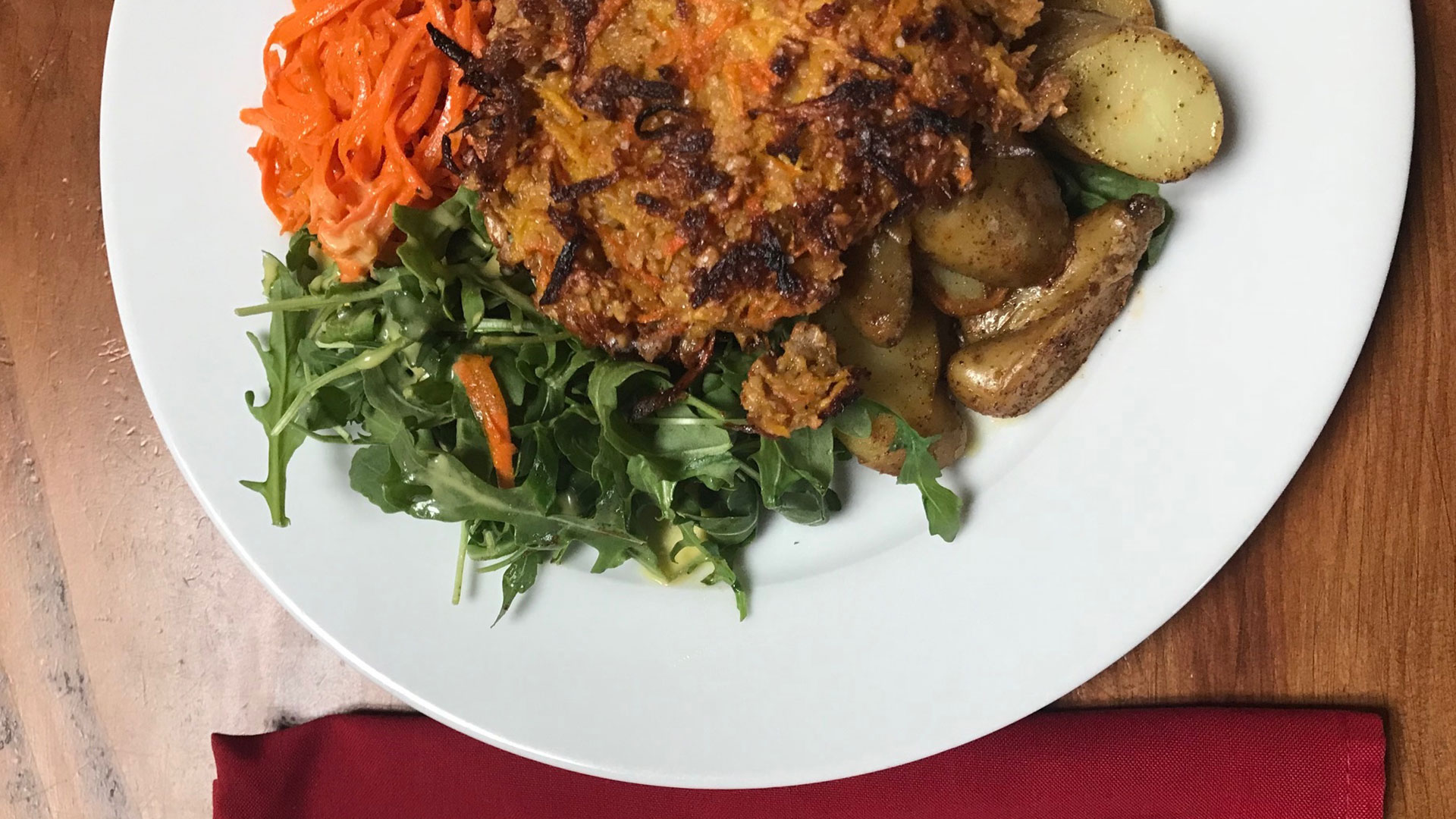 Pan-fried vegetable cake with greens and carrots on a white plate.