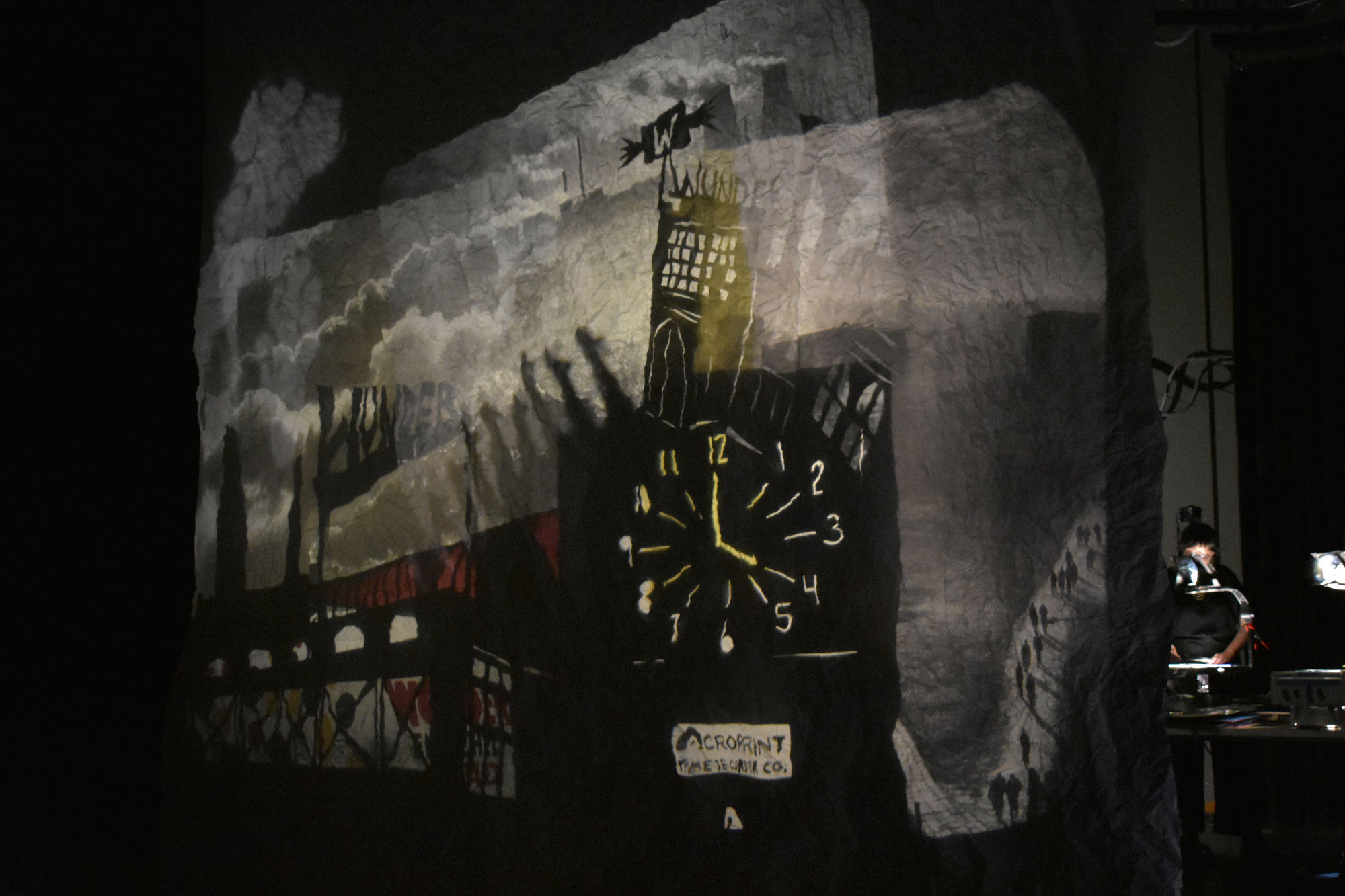 Projected images of clocktower on scrim with person looking down on overhead projector behind