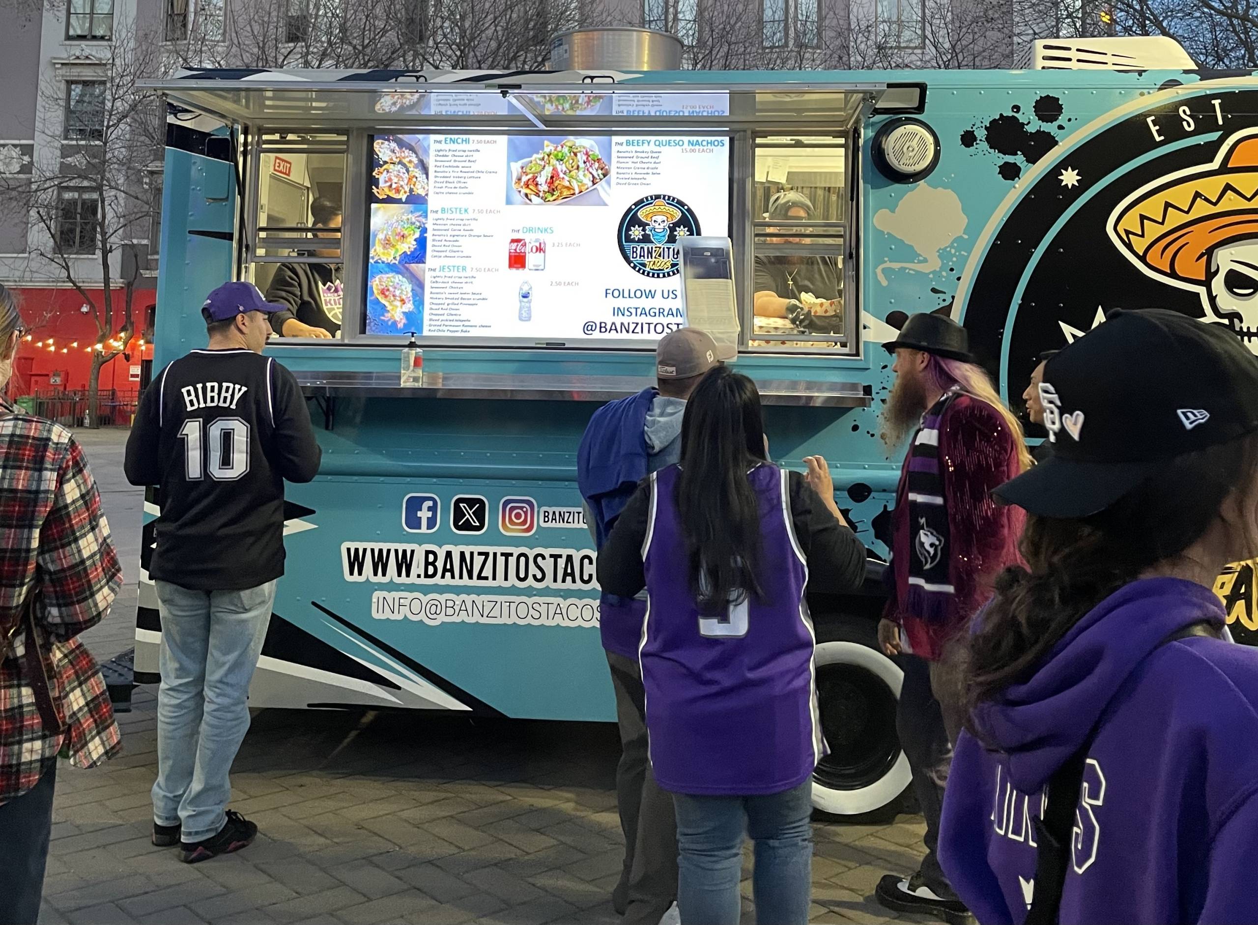 a group of Sacramento Kings basketball fans wait in line to order tacos from a truck outside of the team's arena
