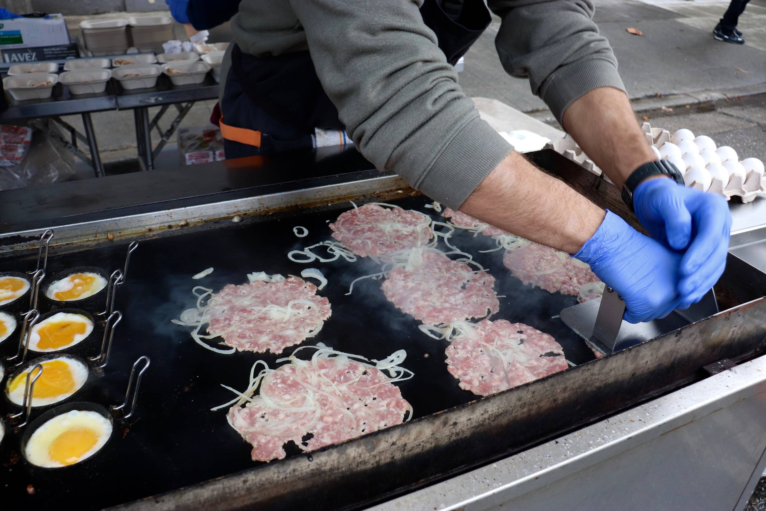 an outdoor cook smashes sausage patties into a searing grill