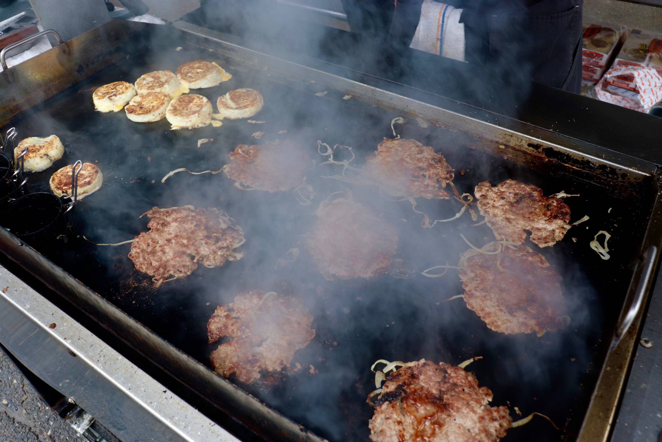 a portable griddle sizzles with sausage patties, onions and eggs