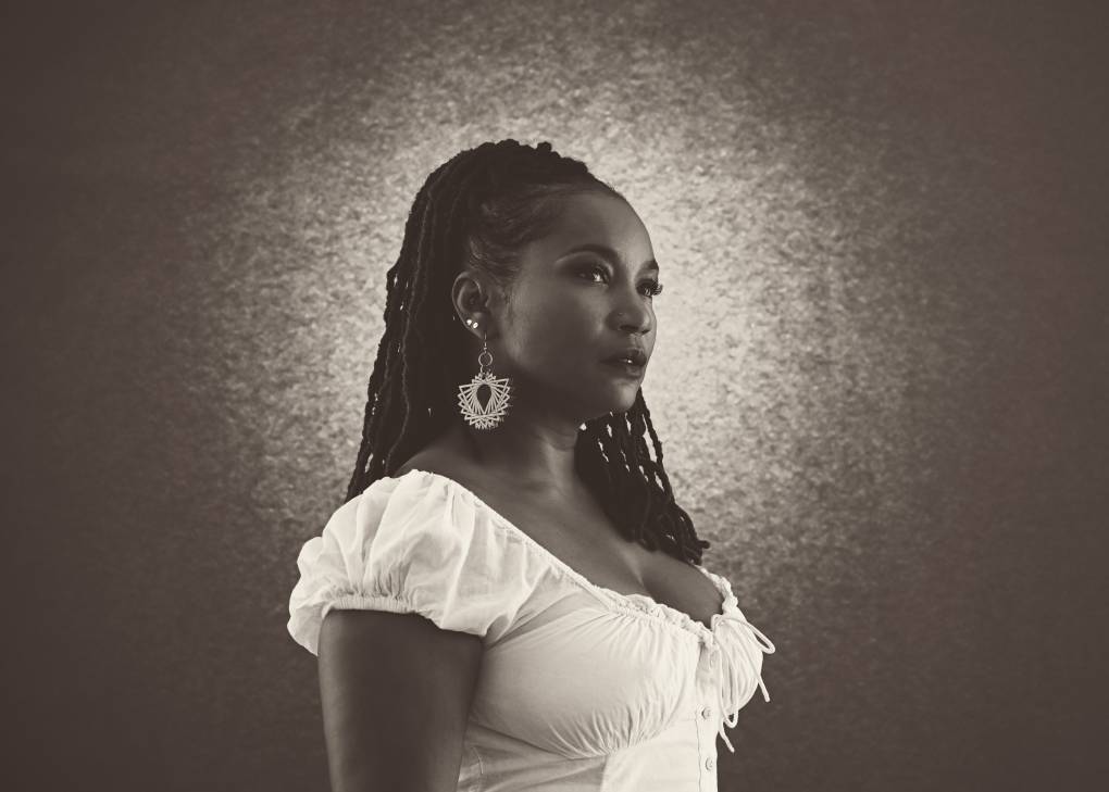 A black and white profile shot of a Black women with long dreadlocks in a white dress.