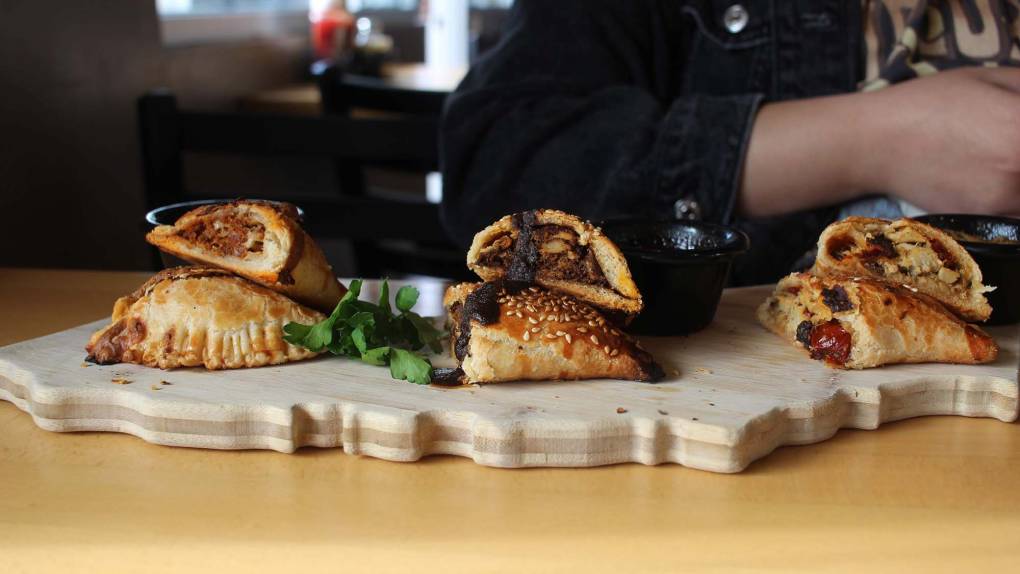 On a wooden cutting board, three empanadas cut open to show the fillings inside.