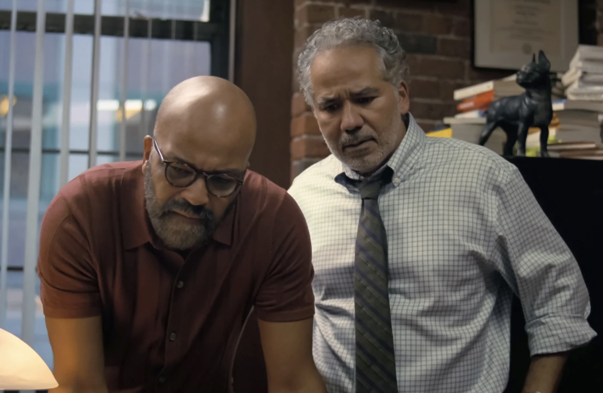 A Black man in a polo shirt and a Latino man in a shirt and tie both peer down at a desk looking concerned.