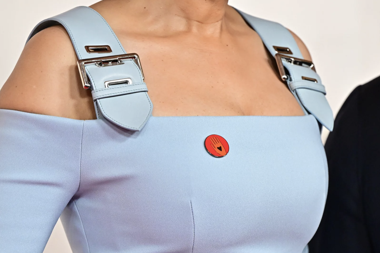 A close up of a blue dress with chunky belt-like straps. There is a red pin on the front.