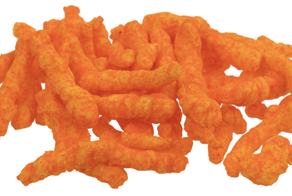 A pile of cheeto-like snacks sit in a pile on a white background.
