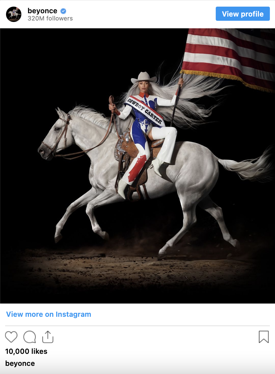 A Black woman dressed in red, white and blue sits side saddle on a galloping white horse, holding up an American flag.