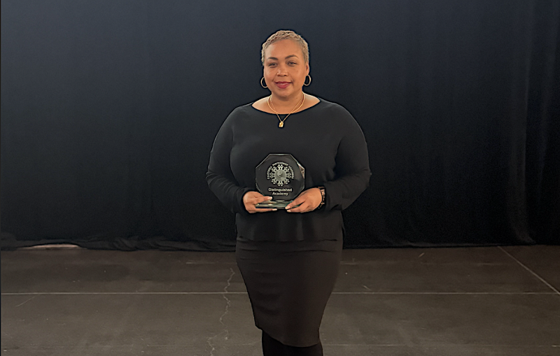 An academic director stands on stage holding an award.