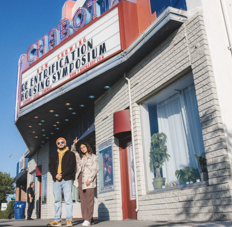 Two filmmakers pose in front of a theater marquee.