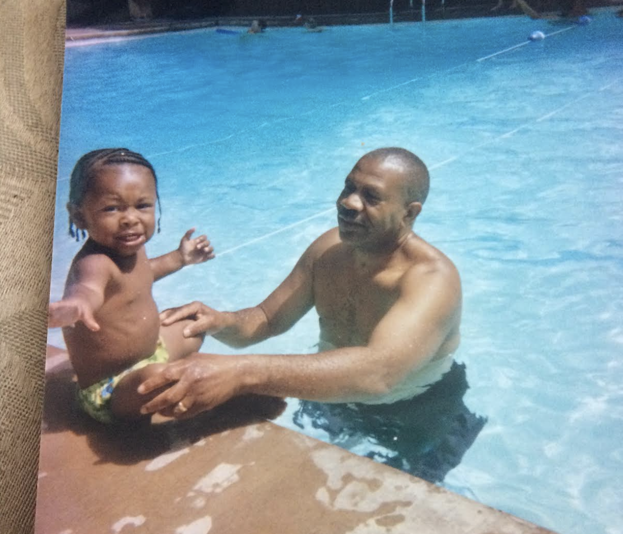 Dwayne Davis as a baby, sitting poolside as his grandfather Lenny Williams stands in the pool with his arms holding onto the young child.