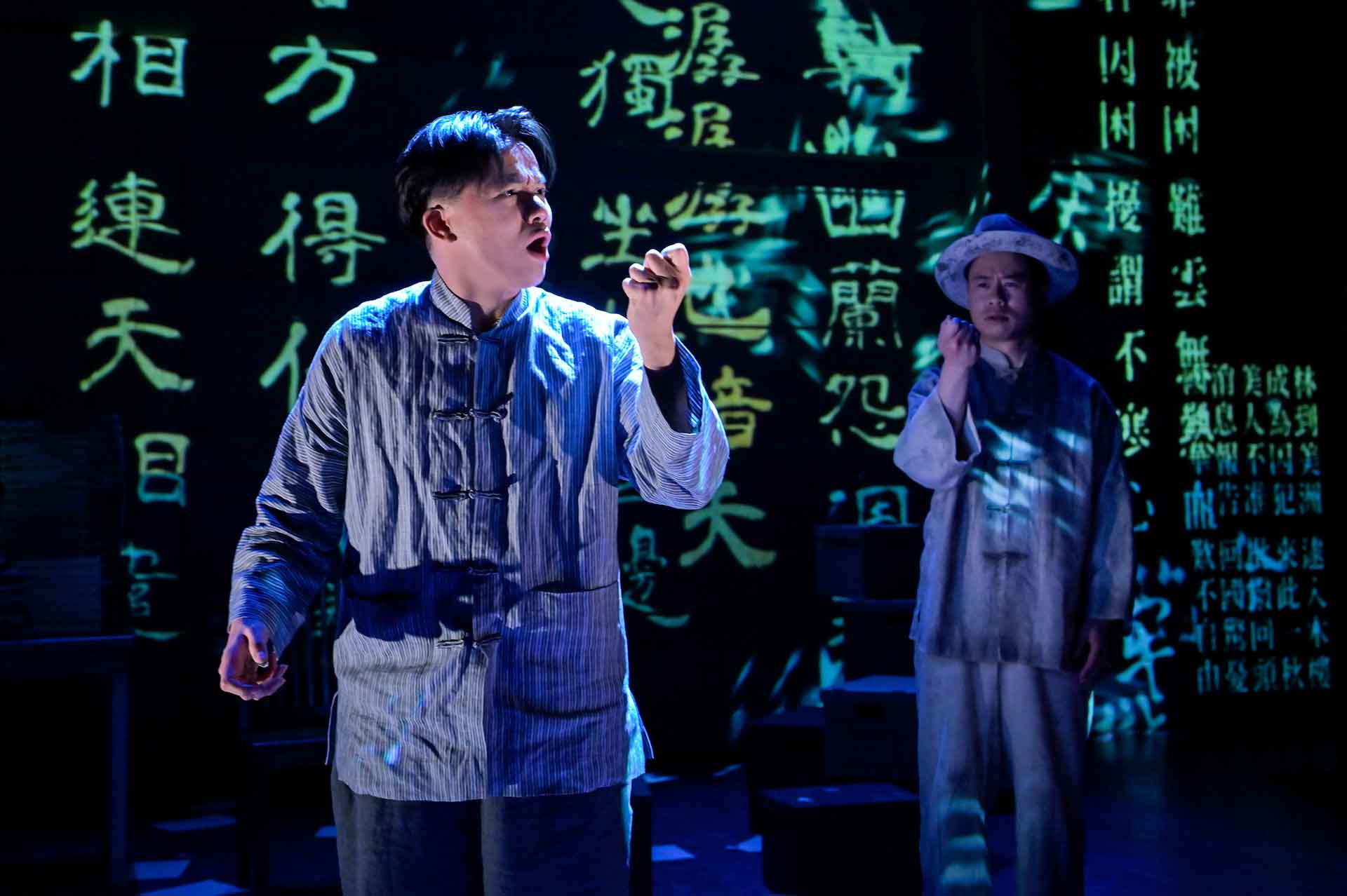 A Chinese man speaks while determinedly making a fist against a backdrop of black with bright green Chinese lettering