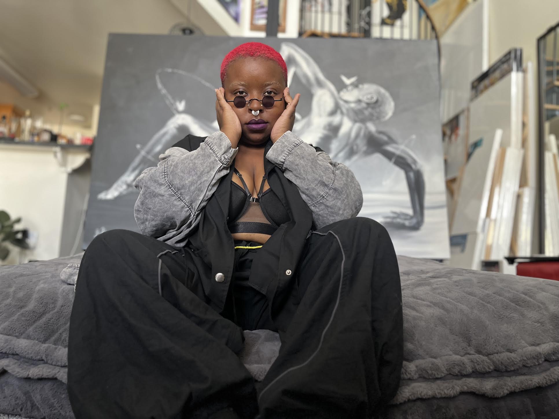 Multitalented artist Zoë Boston sits on a cushion in front of a black and white painting of hers.