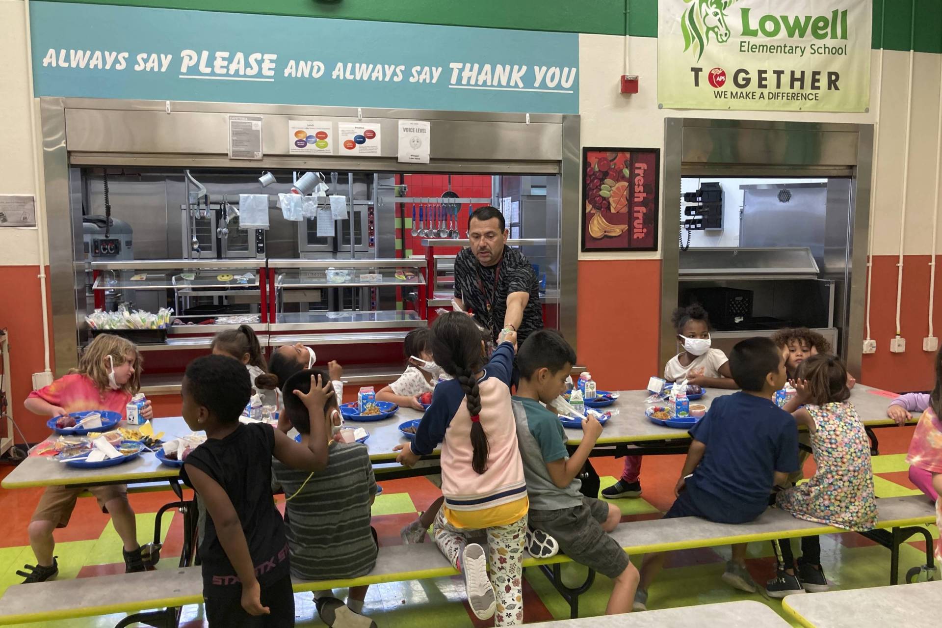 An adult hands out food to children in a canteen.