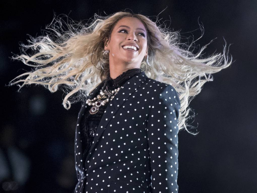 A Black woman on stage smiling with her long blonde hair blowing in the wind.