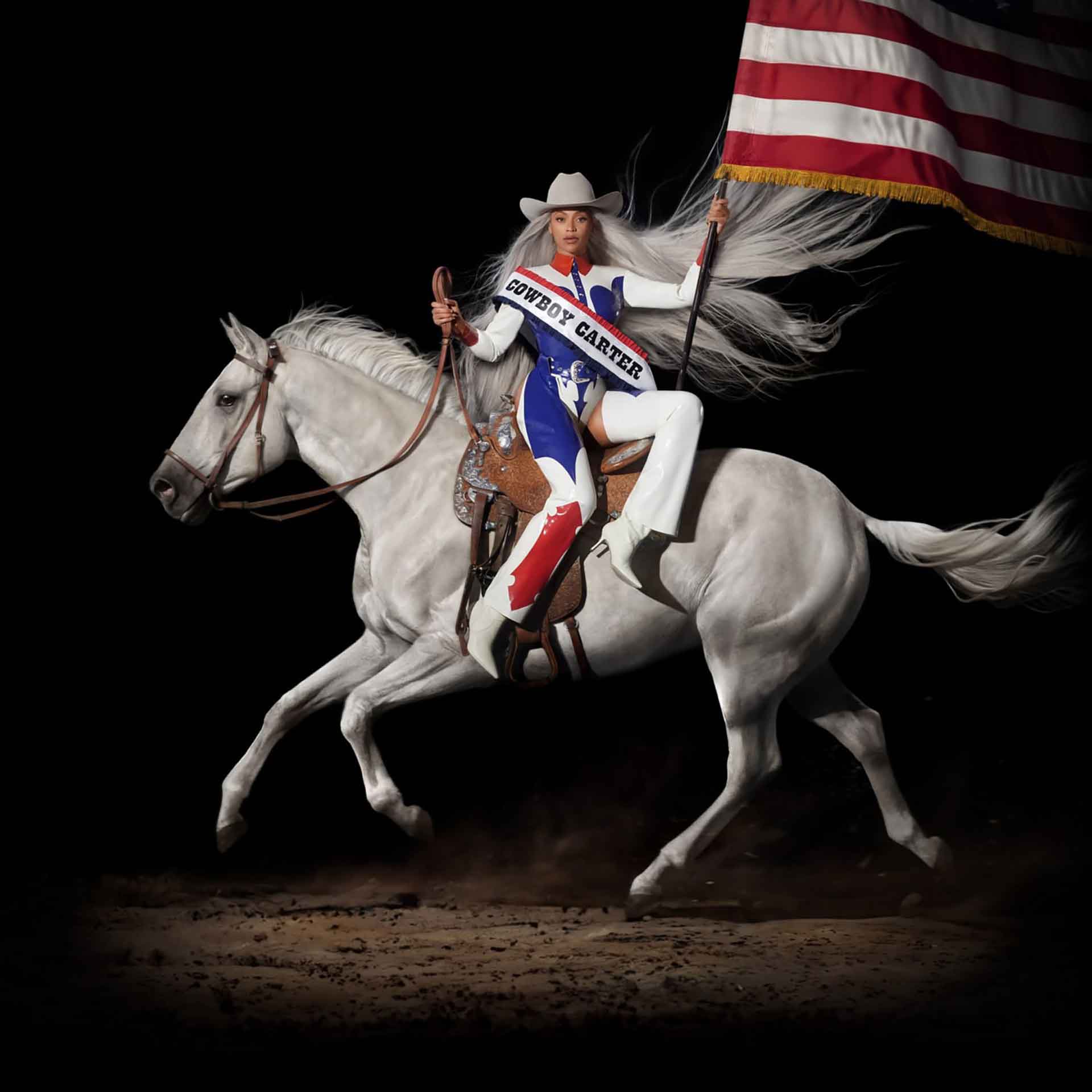A woman in red white and blue clothes, with a sash reading 'Cowboy Carter,' sitting side saddle on a horse and holding an American flag