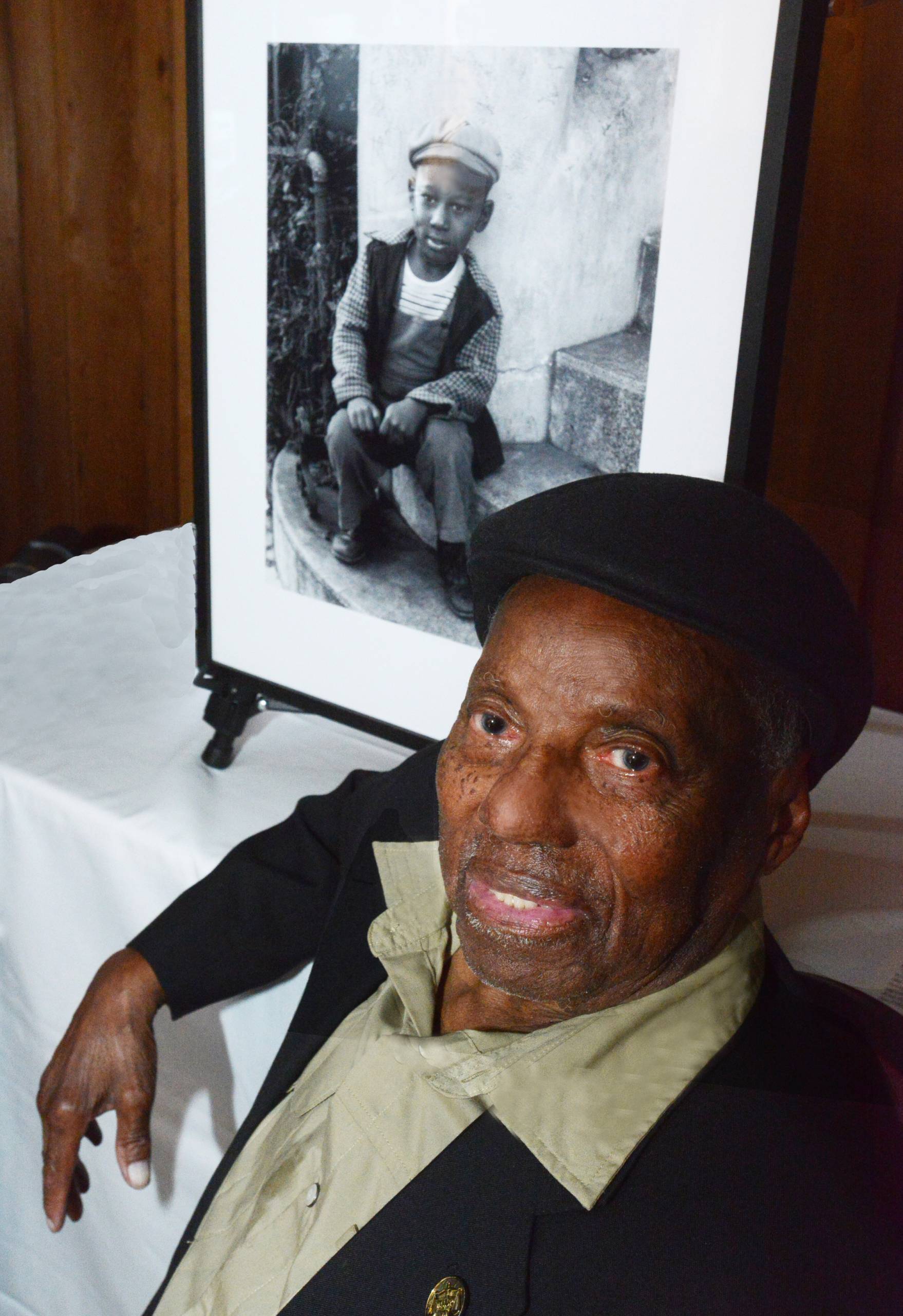 Portrait of older person sitting in front of framed photo of young person