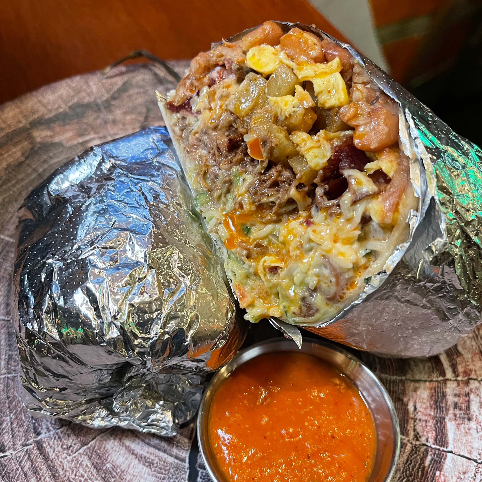 Foil-wrapped breakfast burrito cut in half to show its cheesy interior. A tub of orange salsa on the side.