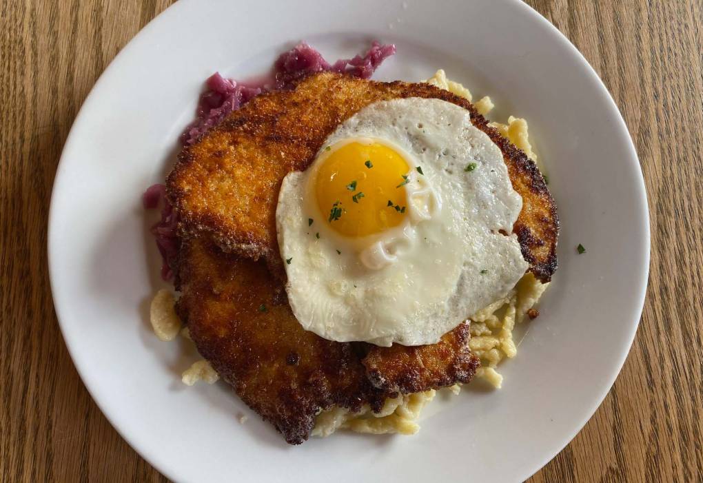 German pork schnitzel topped with a fried egg, on a white plate.