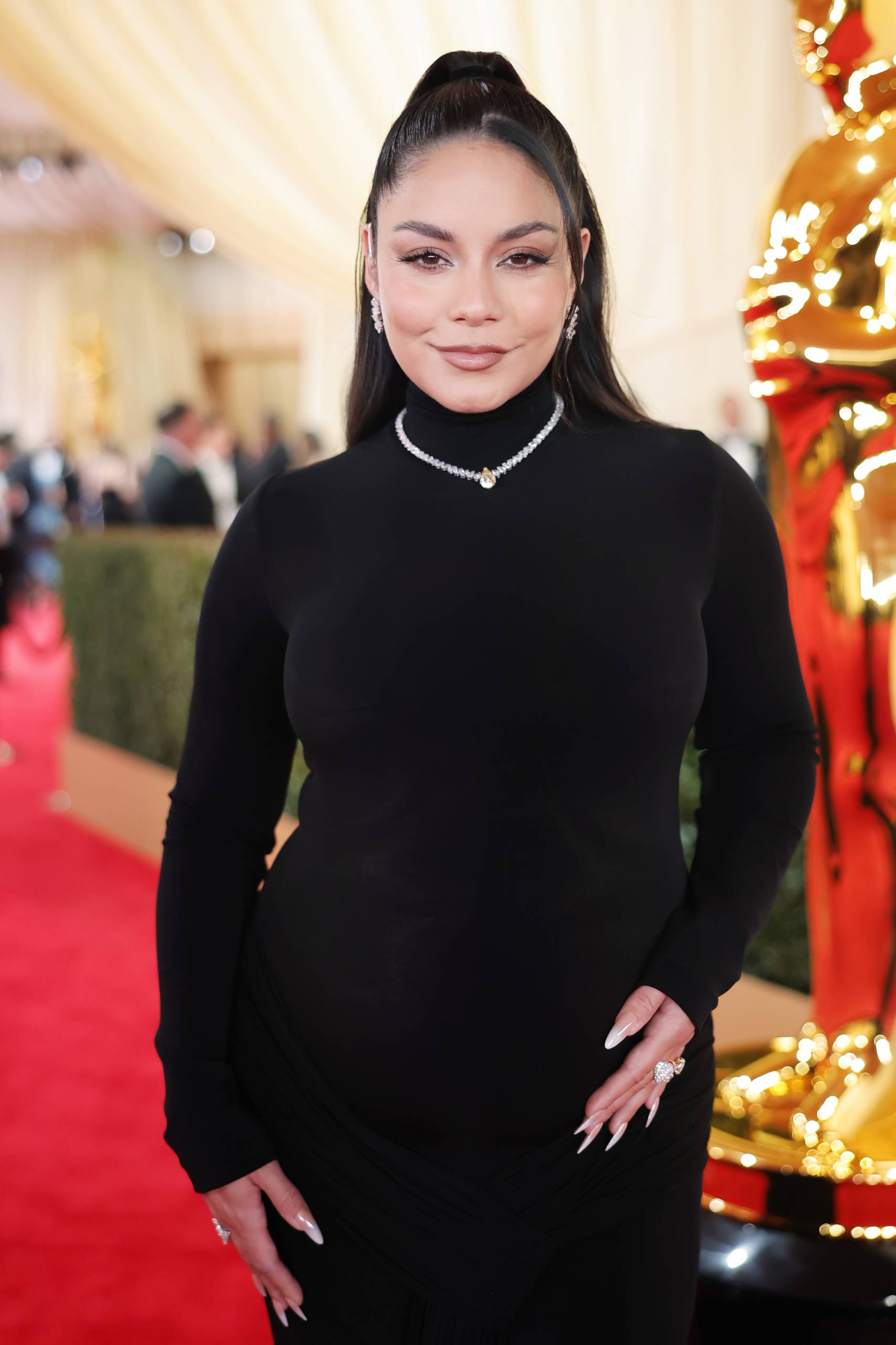 A pregnant woman wearing a black form fitting, long sleeved, high necked gown.