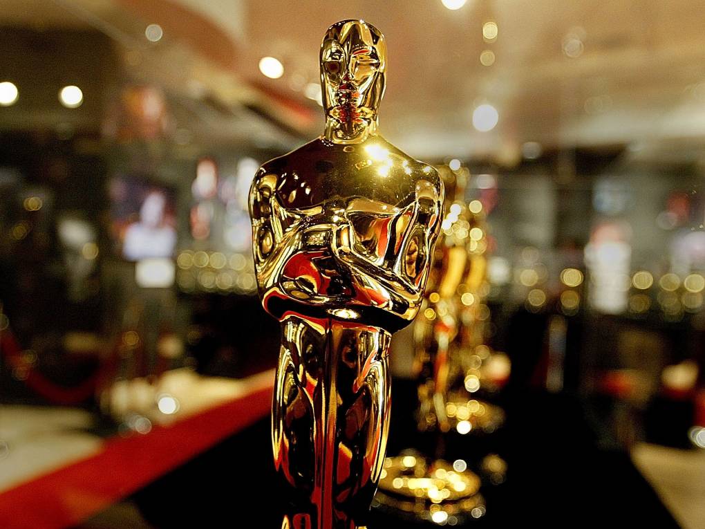 A gold Oscars statue in close up, standing in a long line of awards.